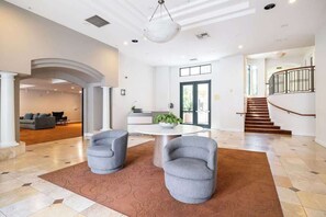 A spacious lobby with a central seating area, a staircase, and a view of the outdoor area.