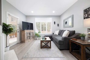 A living room with a sofa, a coffee table, a television, and a window with blinds.