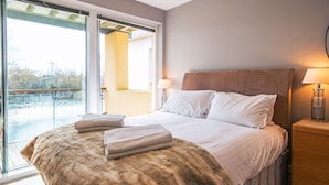 Une chambre avec un grand lit, deux lampes de chevet, une table de nuit en bois et une vue sur l’extérieur, accessible par une porte vitrée.