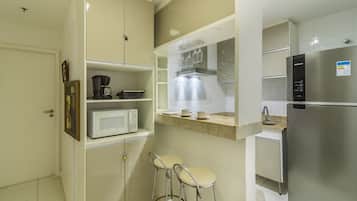 Cocina compacta con microondas, cafetera y electrodomésticos de acero inoxidable. Hay dos taburetes de bar y una pequeña encimera con lavabo.