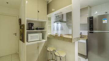 A compact kitchen with a microwave, coffee maker, and stainless steel appliances. There are two bar stools and a small countertop with a sink.