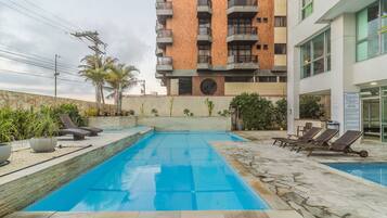 Piscina com espreguiçadeiras, cercada por um muro de pedra e plantas.