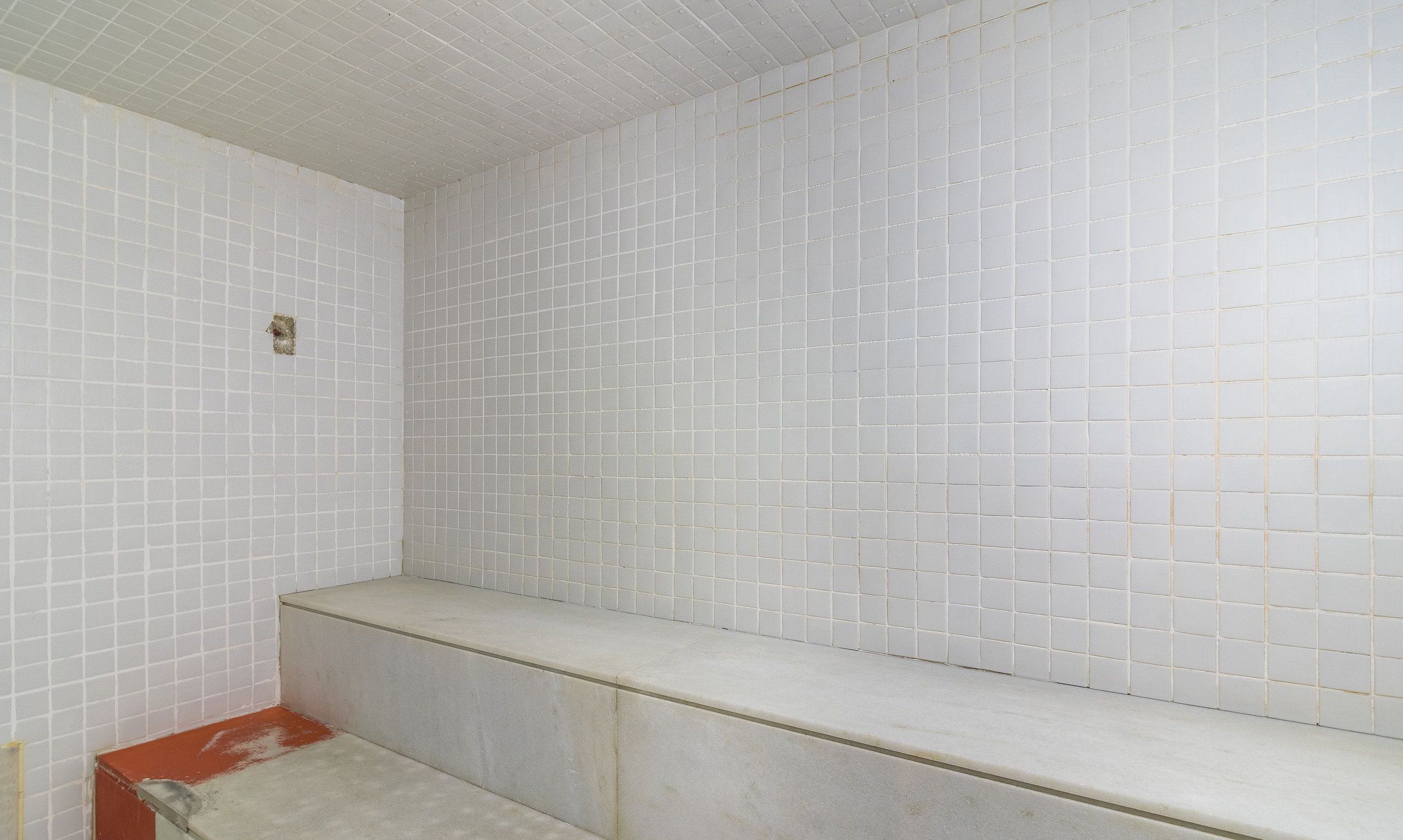 A bathroom with white tiled walls and a bench.