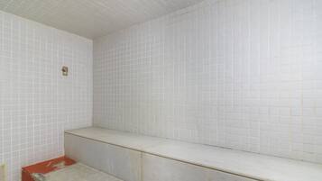 A bathroom with white tiled walls and a bench.