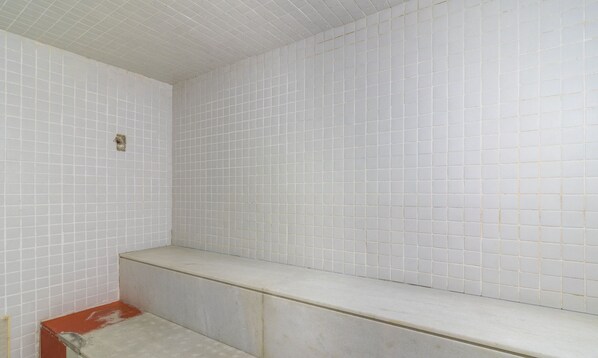 Un baño con paredes de azulejos blancos y un banco.