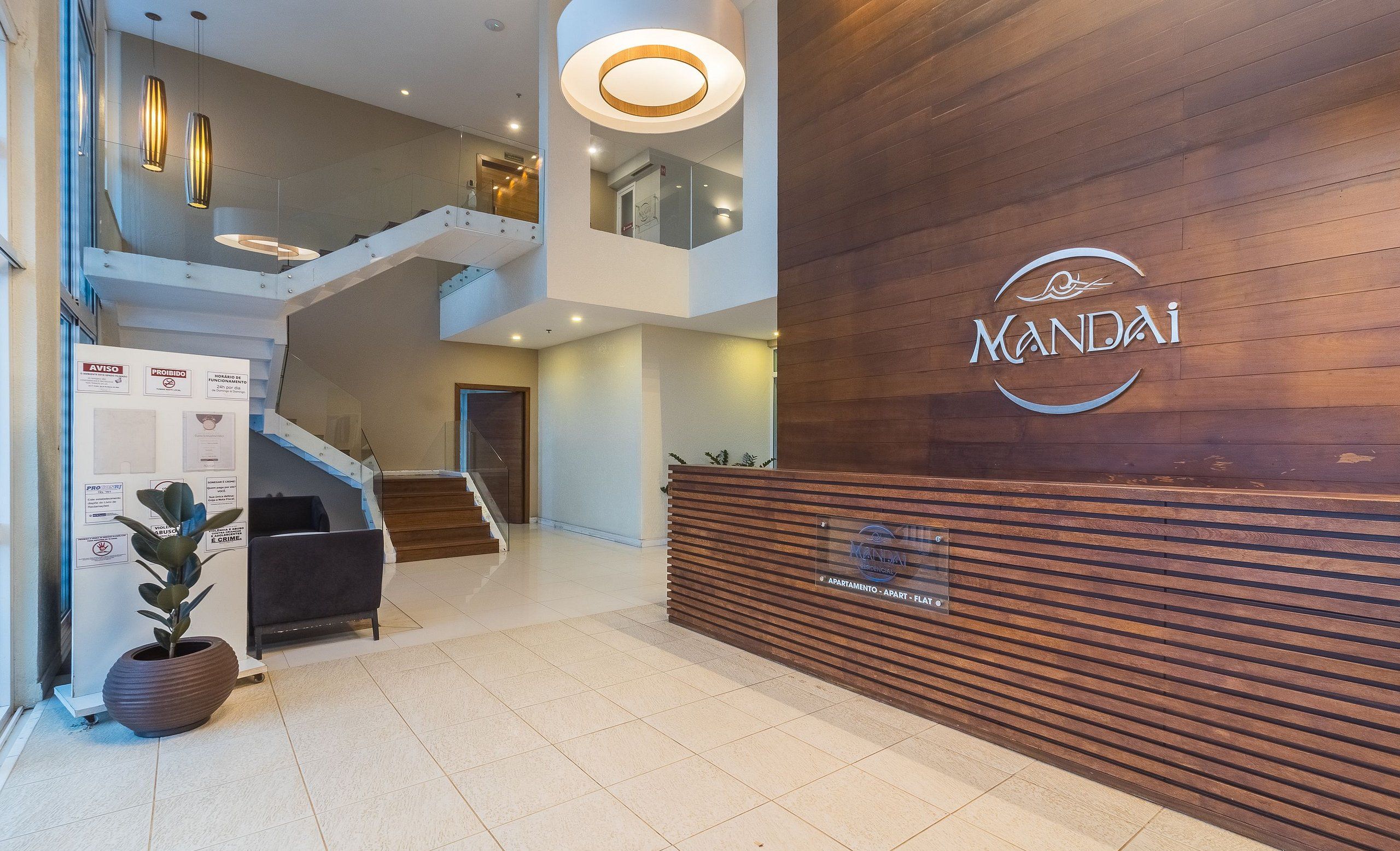 A modern lobby with a wooden reception desk, a staircase, and a potted plant.