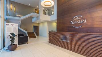 A modern lobby with a wooden reception desk, a staircase, and a potted plant.