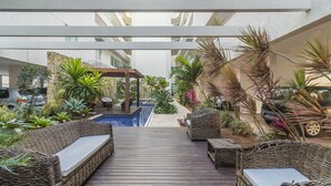 Een overdekte buitenruimte met een zwembad, rieten meubels en verschillende planten.