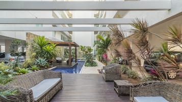 Un espacio al aire libre cubierto con piscina, mobiliario de mimbre y diversas plantas.