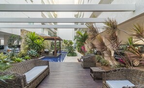A covered outdoor area with a pool, wicker furniture, and various plants. - 1 Bedroom Apartment in Oceanfront Condo Mnda0217 (Cabo Frio)