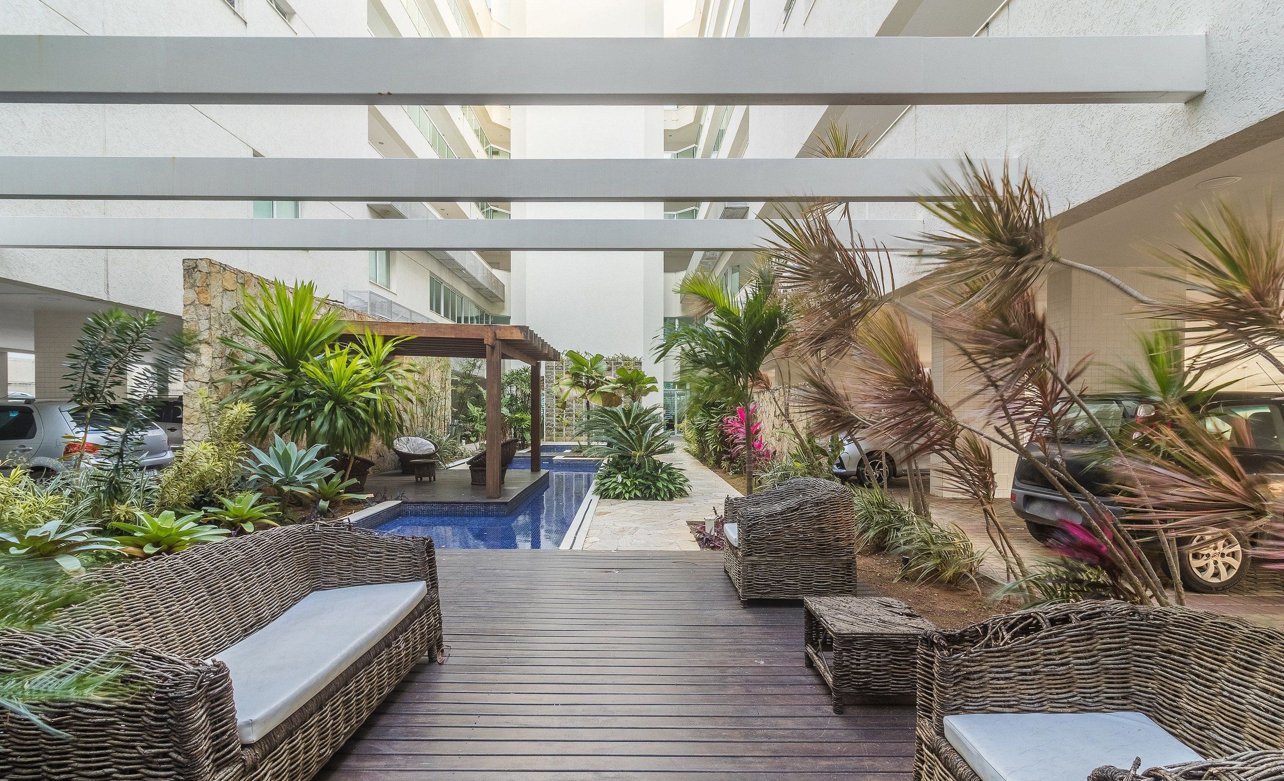 Espaço coberto ao ar livre com piscina, móveis de vime e diversas plantas.