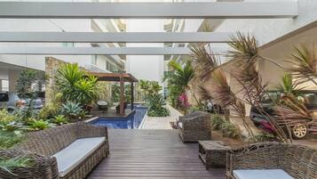 Espaço coberto ao ar livre com piscina, móveis de vime e diversas plantas.