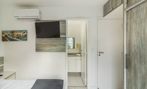 Une chambre à coucher avec un lit, un téléviseur fixé au mur, un tableau et une porte donnant sur une salle de bain.
