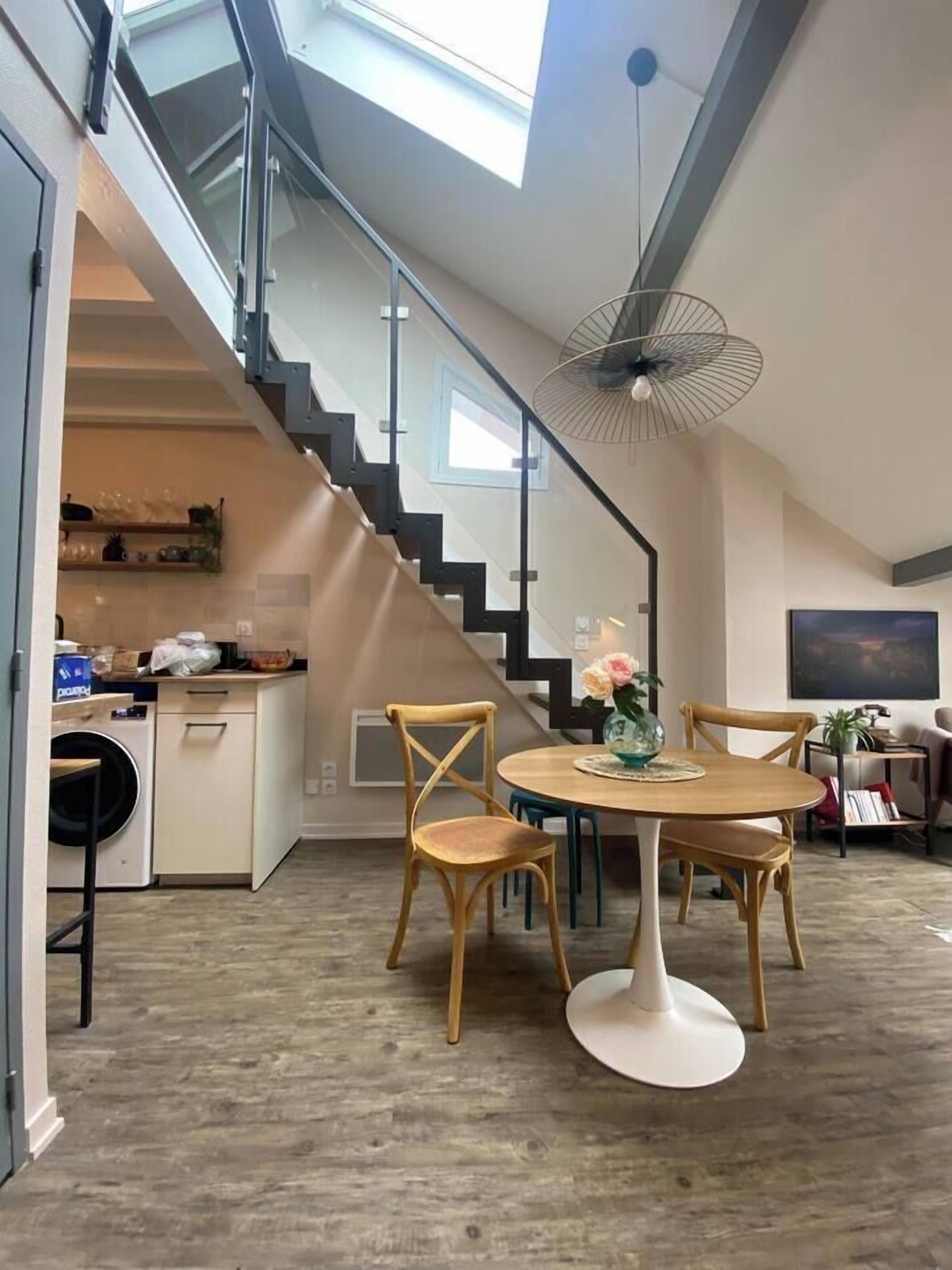 Een moderne keuken met een ingebouwde wasmachine, een eethoek met een ronde tafel en stoelen, en een trap naar een verdieping erboven.