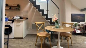 A modern kitchen with a built-in washing machine, a dining area with a round table and chairs, and a staircase leading to an upper level. - Stylish & Cosy Mezzanine in Historical Old Town (Annecy)