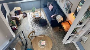 A modern living room with a sofa, coffee table, and a hanging chair. There is a staircase leading to an upper level. - Stylish & Cosy Mezzanine in Historical Old Town (Annecy)