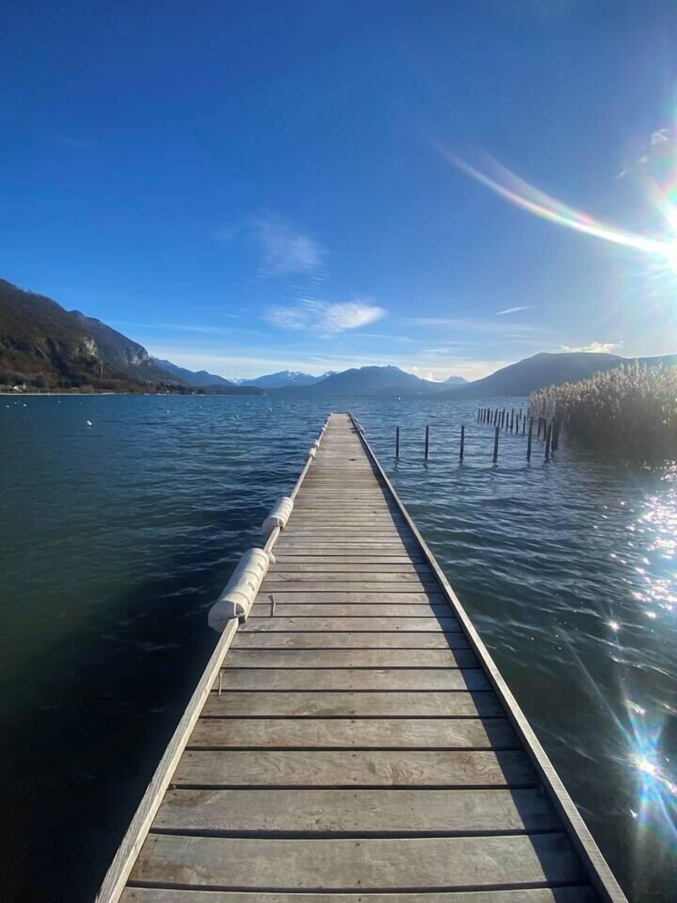 A wooden pier extending into calm water, surrounded by mountains and clear skies.