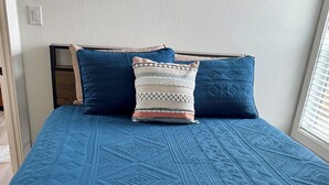 Un llit amb un sobreblau acolxat, un coixí blanc i amb dibuixos, i una manta beix.