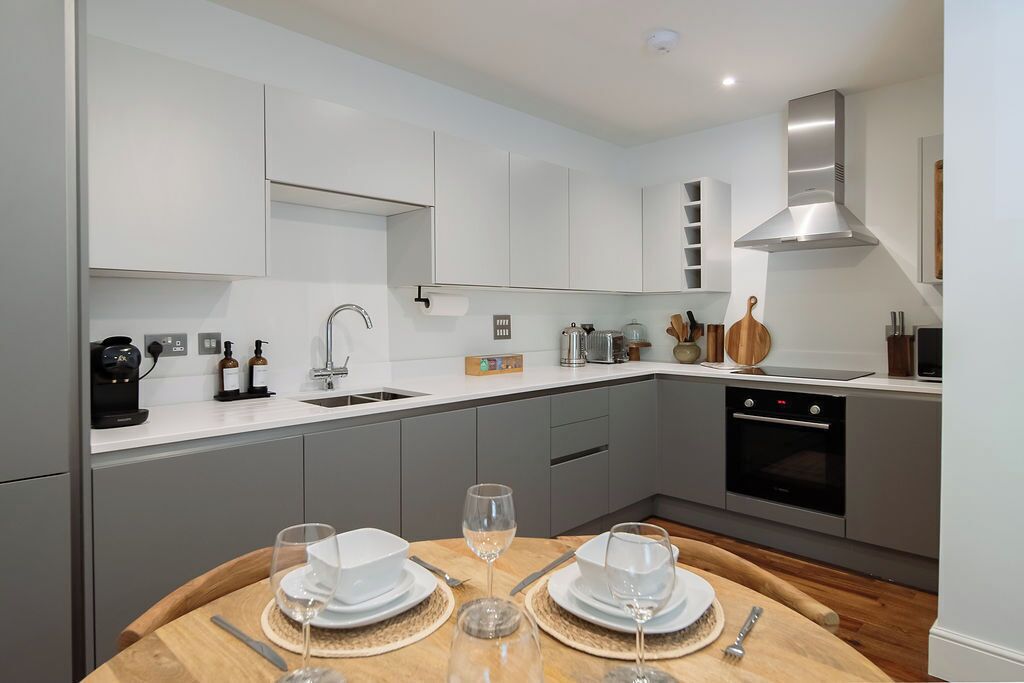 A modern kitchen with white cabinets, a stainless steel range hood, and a dining area with a wooden table set for two.