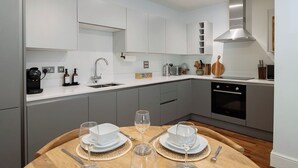 Una cocina moderna con armarios blancos, una campana extractora de acero inoxidable y una zona de comedor con una mesa de madera dispuesta para dos personas.