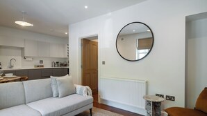 Una sala moderna con un sofá gris, una mesita redonda y un espejo circular en la pared.