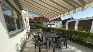 Un patio al aire libre con mesa y sillas, un espacio cubierto y vistas de edificios cercanos.