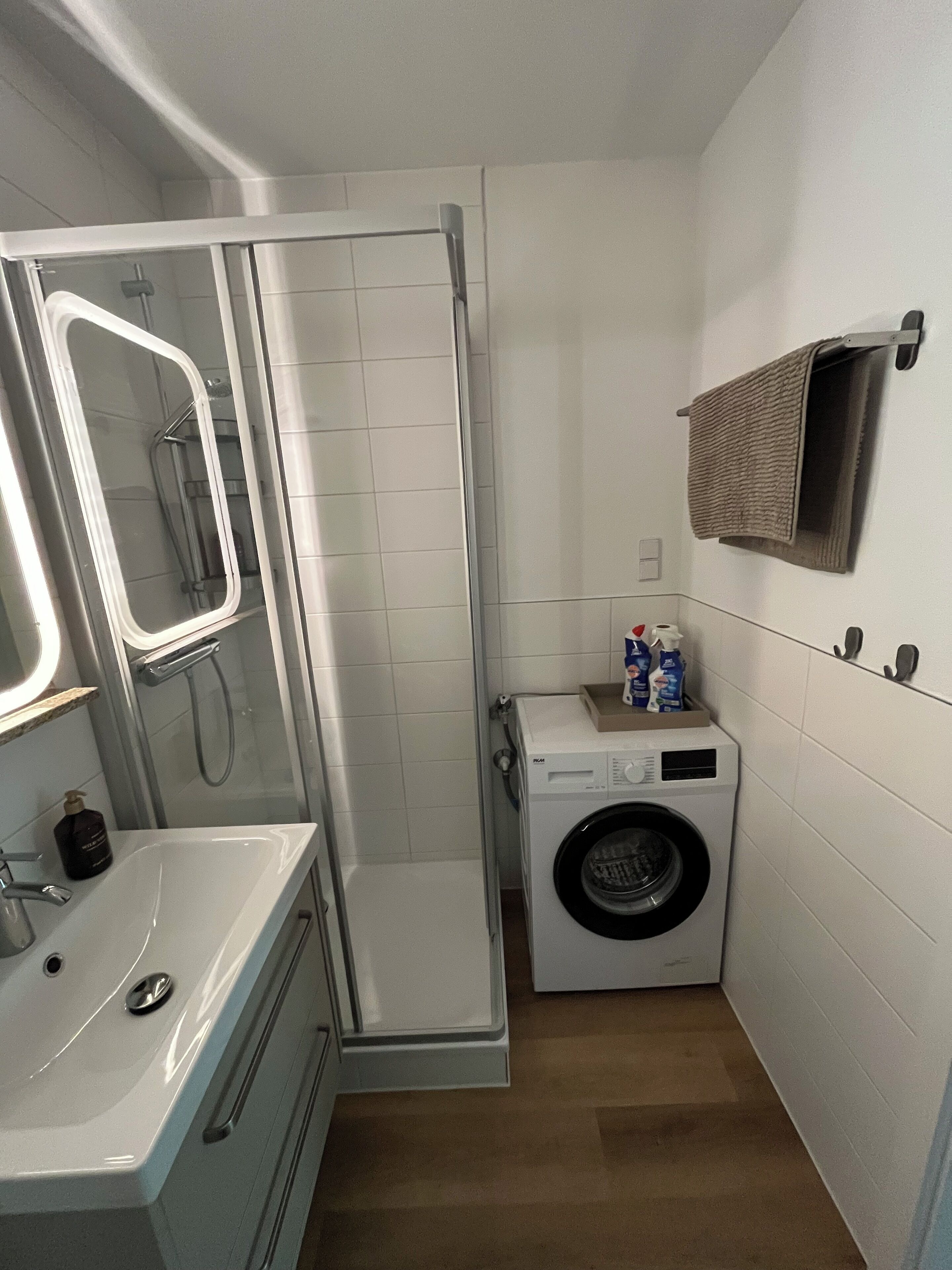 Une salle de bain compacte dotée d’une douche à parois de verre, d’un lavabo, d’un lave-linge et d’un porte-serviettes.