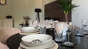 Une table à manger dressée avec de l’assiette blanche, des bols et des verres transparents, entourée de chaises en osier.