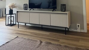 Un salon moderne avec un téléviseur à écran plat posé sur une console blanche, trois œuvres d’art encadrées au-dessus du téléviseur et un plancher en bois.