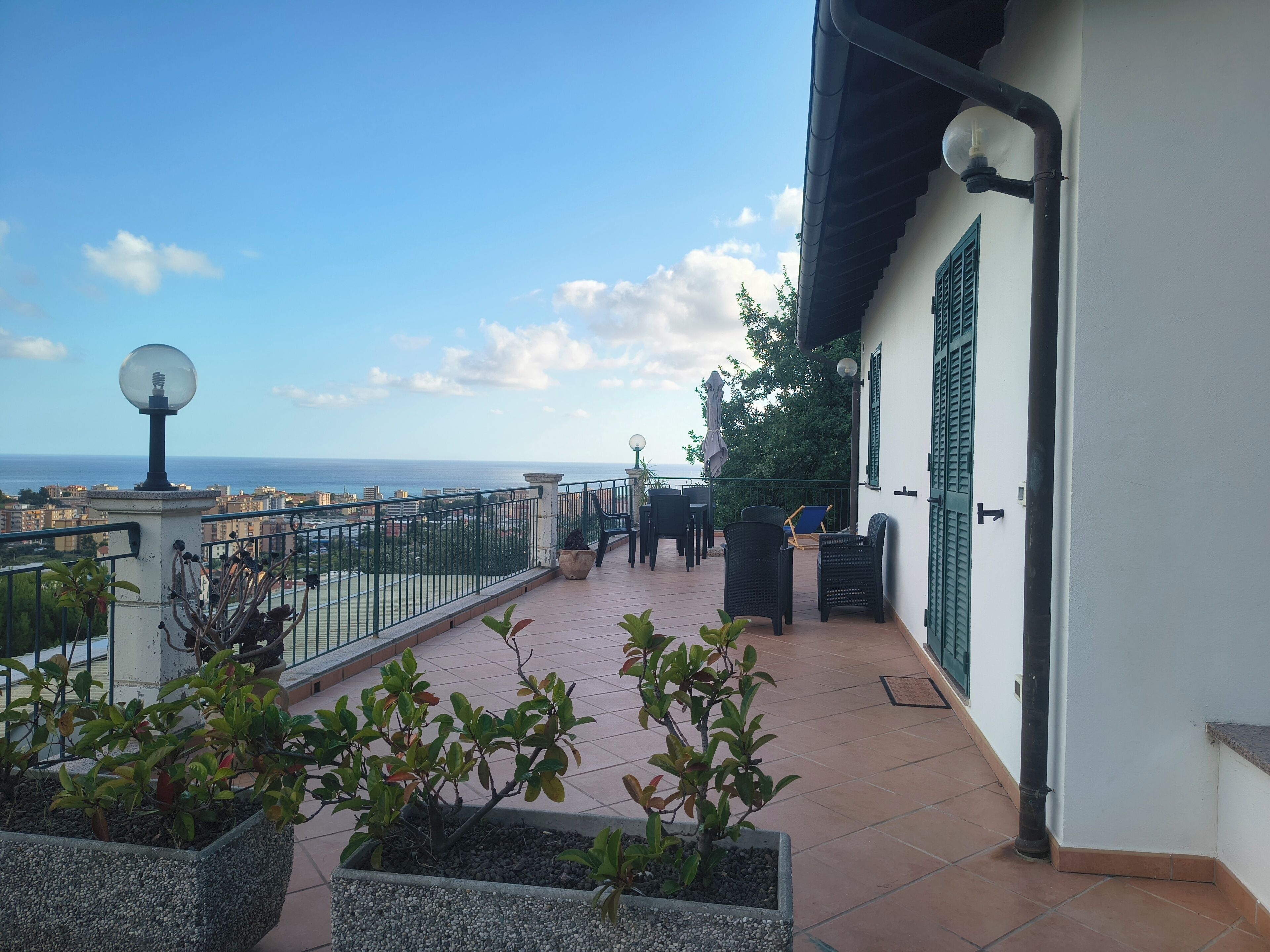 A balcony with a view of the sea, outdoor furniture, and potted plants.