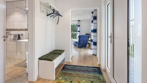 Un couloir avec un banc, un tapis et une vue sur une salle de bain équipée d’une douche et d’un porte-serviettes.