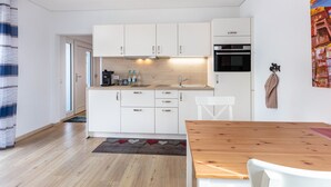 Une cuisine moderne avec des meubles blancs, un plan de travail en bois et un coin repas comprenant une table en bois et des chaises blanches.