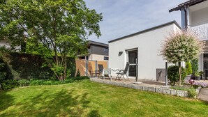 Un immeuble résidentiel moderne doté d’une pelouse bien entretenue, d’un espace extérieur aménagé pour s’asseoir et d’une variété de plantes.