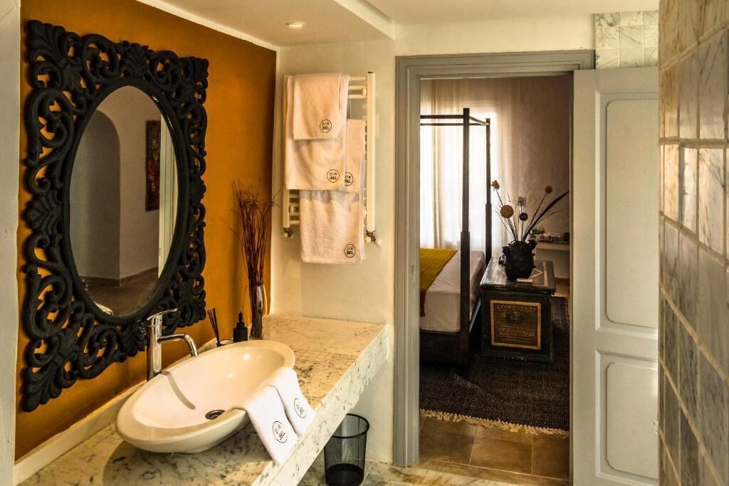 Um banheiro com um espelho grande e decorativo, uma pia branca e um porta-toalhas com várias toalhas.