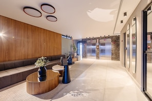 A modern lobby with a wooden wall, a seating area, a round coffee table, and an elevator.
