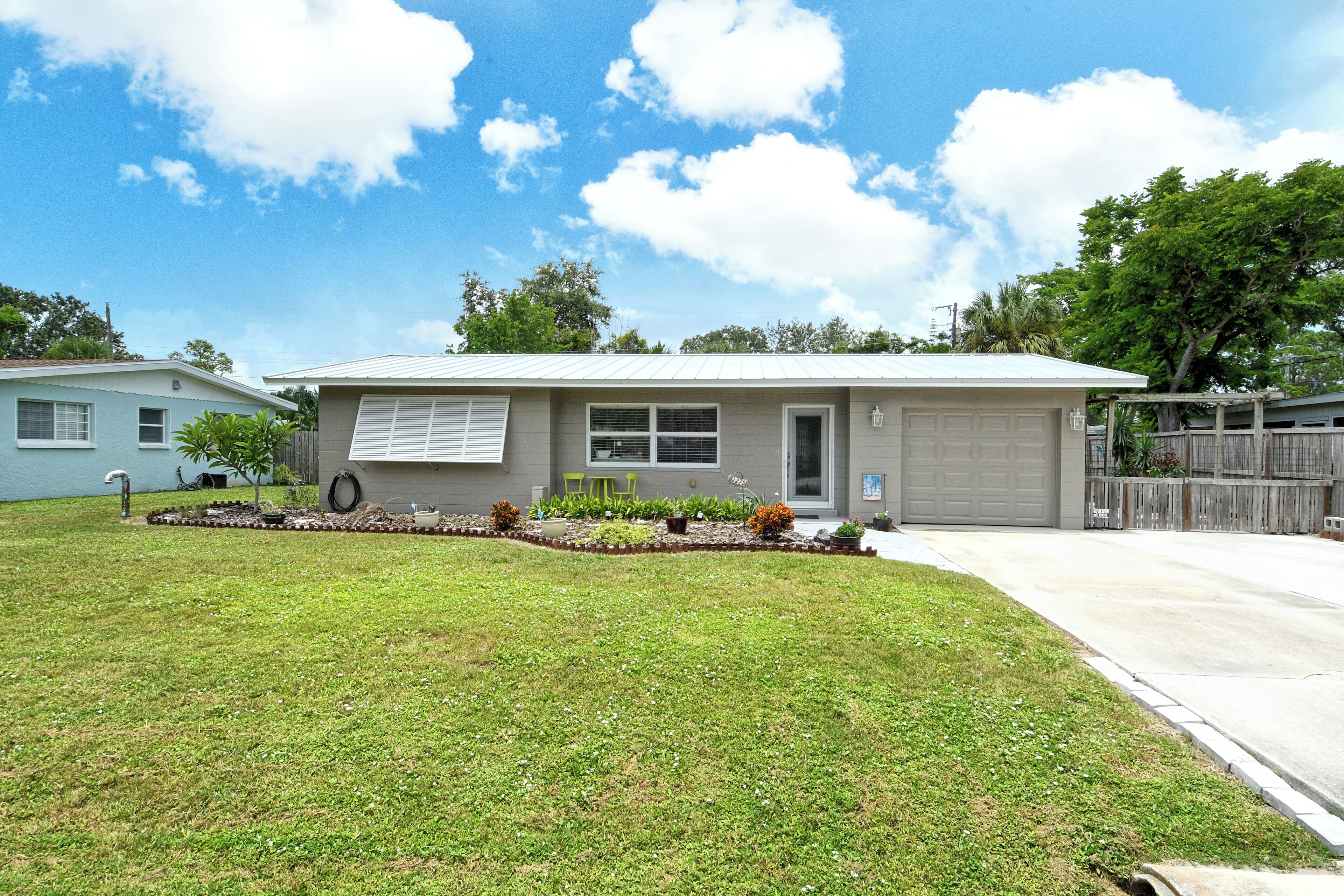 A single-story house with a garage, a front yard with a lawn and small garden, and a clear sky.