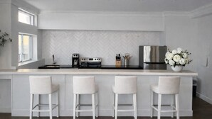 A modern kitchen with a herringbone tile backsplash, stainless steel appliances, and a white island with bar stools. - Daniella's Suites (Peabody)