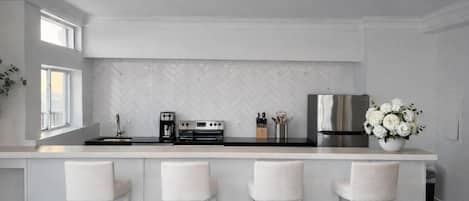 Una cocina moderna con salpicadero de baldosas en espiga, electrodomésticos de acero inoxidable y una isla blanca con taburetes de bar.