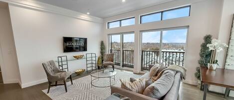 A spacious living room with a large window, a sofa, a coffee table, and a TV mounted on the wall.