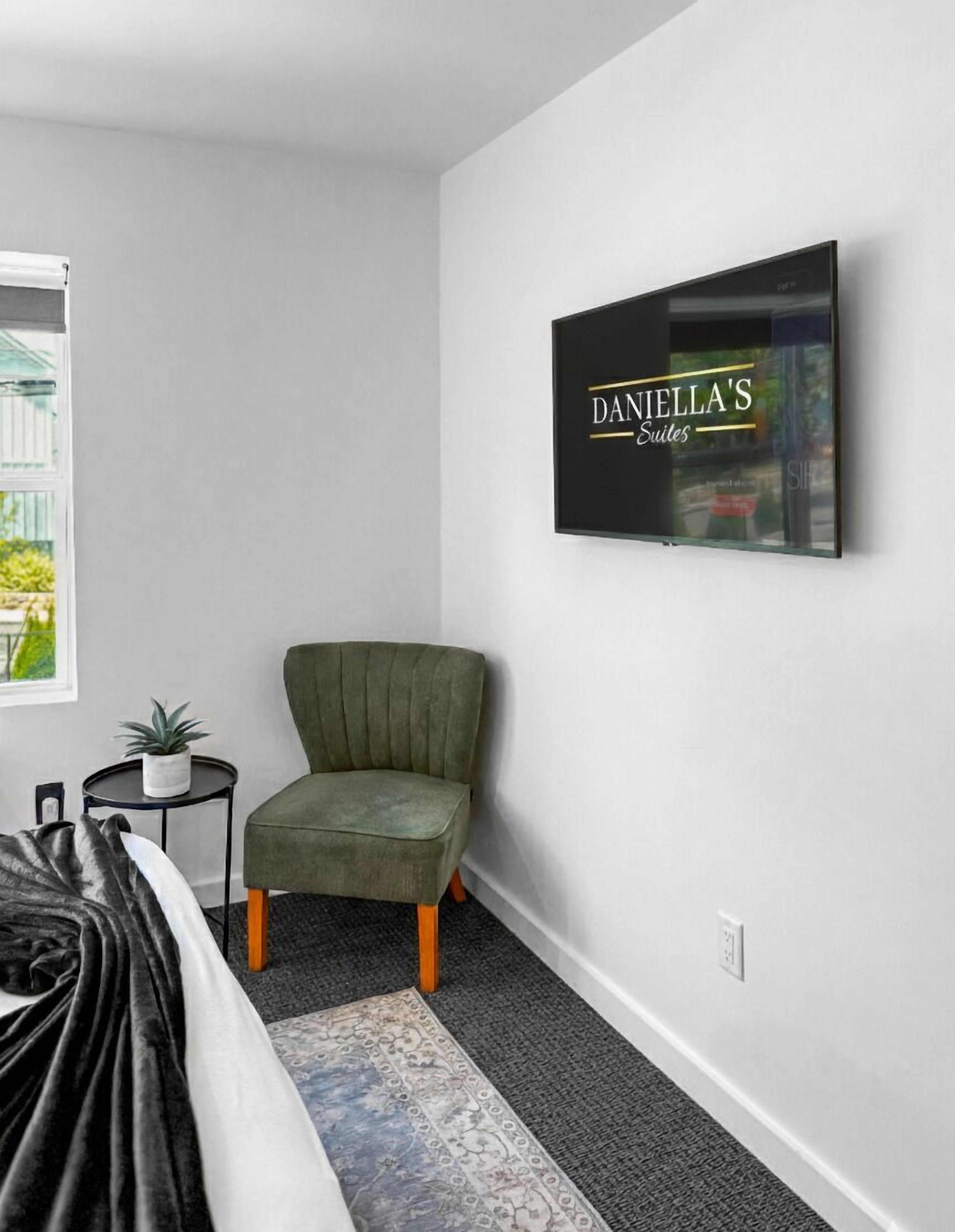 A modern room with a green armchair, a small round table with a plant, a framed sign on the wall, and a patterned rug.