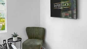 A modern room with a green armchair, a small round table with a plant, a framed sign on the wall, and a patterned rug.