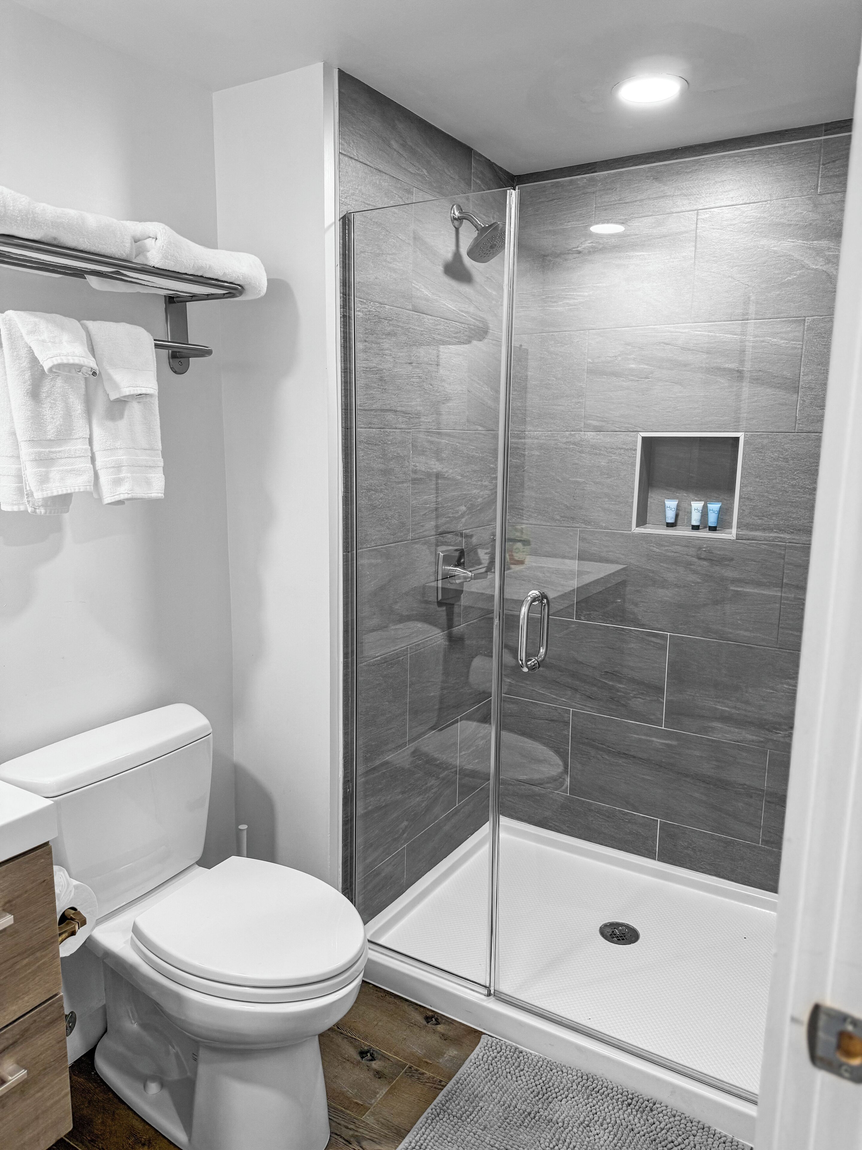 A modern bathroom with a glass-enclosed shower, a white toilet, and a shelf with toiletries.