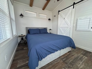 Un dormitorio con cama, una mesita y una ventana con persianas.