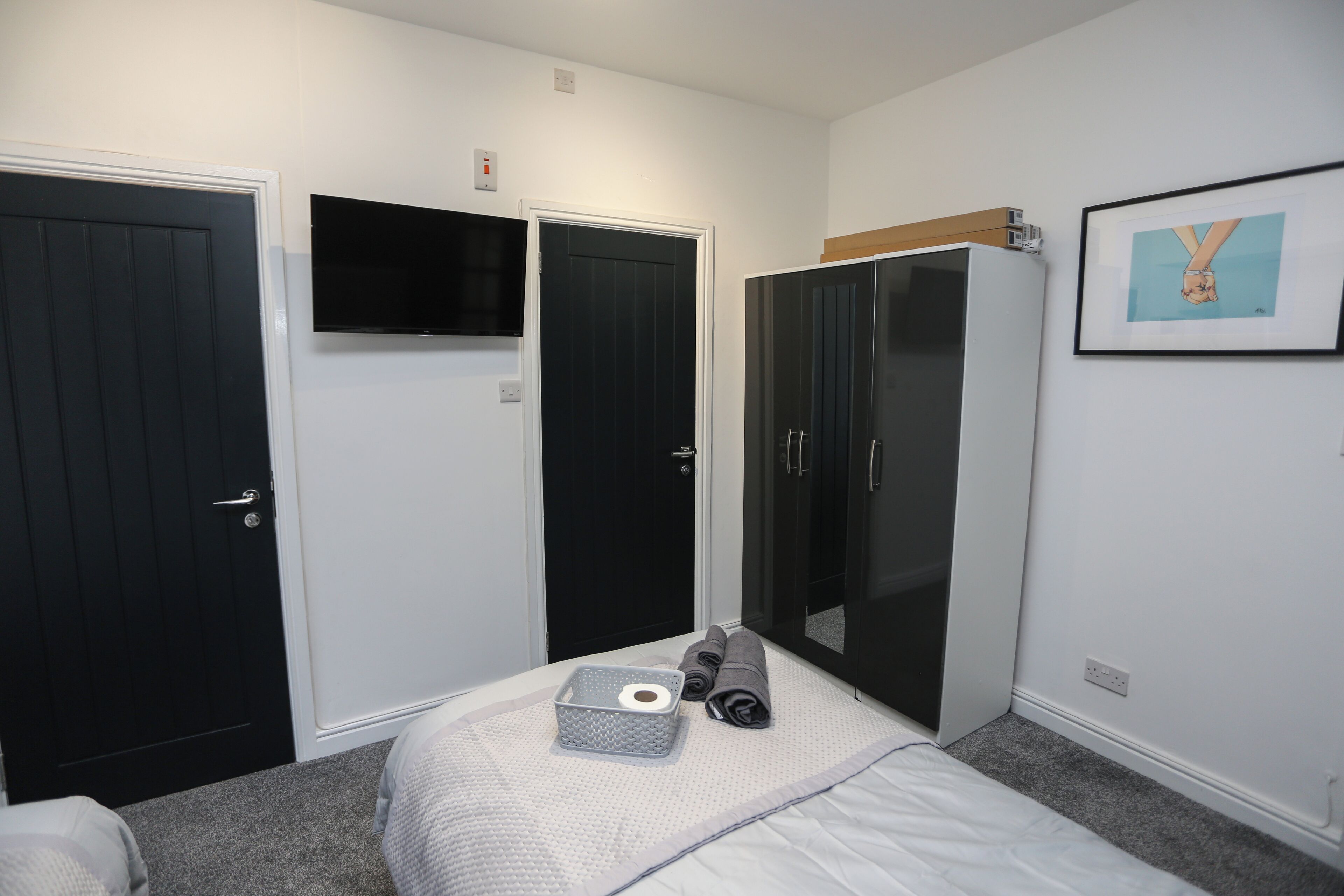 A bedroom with a bed, a TV, a wardrobe, and a framed picture on the wall.