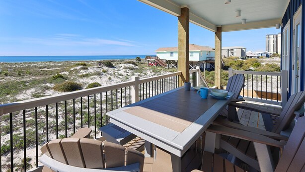 A balcony with a table and chairs overlooking a beach and ocean.