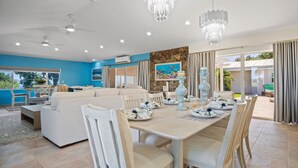 A modern living room with a sofa, dining table, and chairs. There are ceiling fans, a chandelier, and a painting on the wall. - Villa Francisca East-Spacious 3Bedroom Retreat with A/C – Your Perfect Getaway (St Thomas)