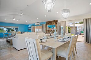 A modern living room with a sofa, dining table, and chairs. There are ceiling fans, a chandelier, and a painting on the wall. - Villa Francisca East-Spacious 3Bedroom Retreat with A/C – Your Perfect Getaway (St Thomas)