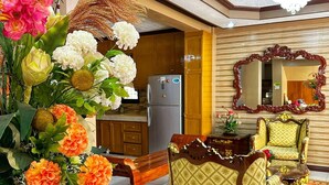 Un salón amplio con un arreglo floral grande, una zona de comedor con mesa y sillas de madera, y una cocina al fondo.