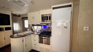 Een kleine keuken met witte kastjes, een magnetron, een koelkast, een fornuis en een spoelbak.