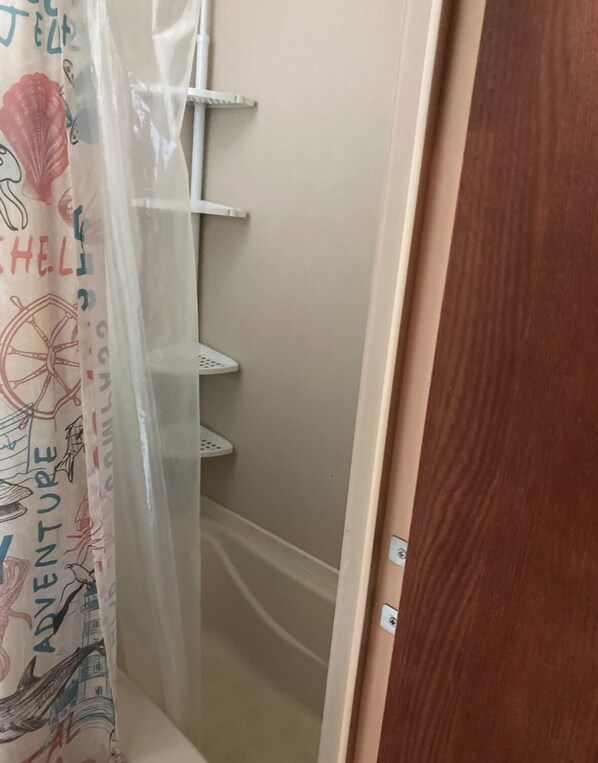 Une salle de bain avec un rideau de douche orné de motifs marins, un porte-serviettes blanc et une porte en bois.